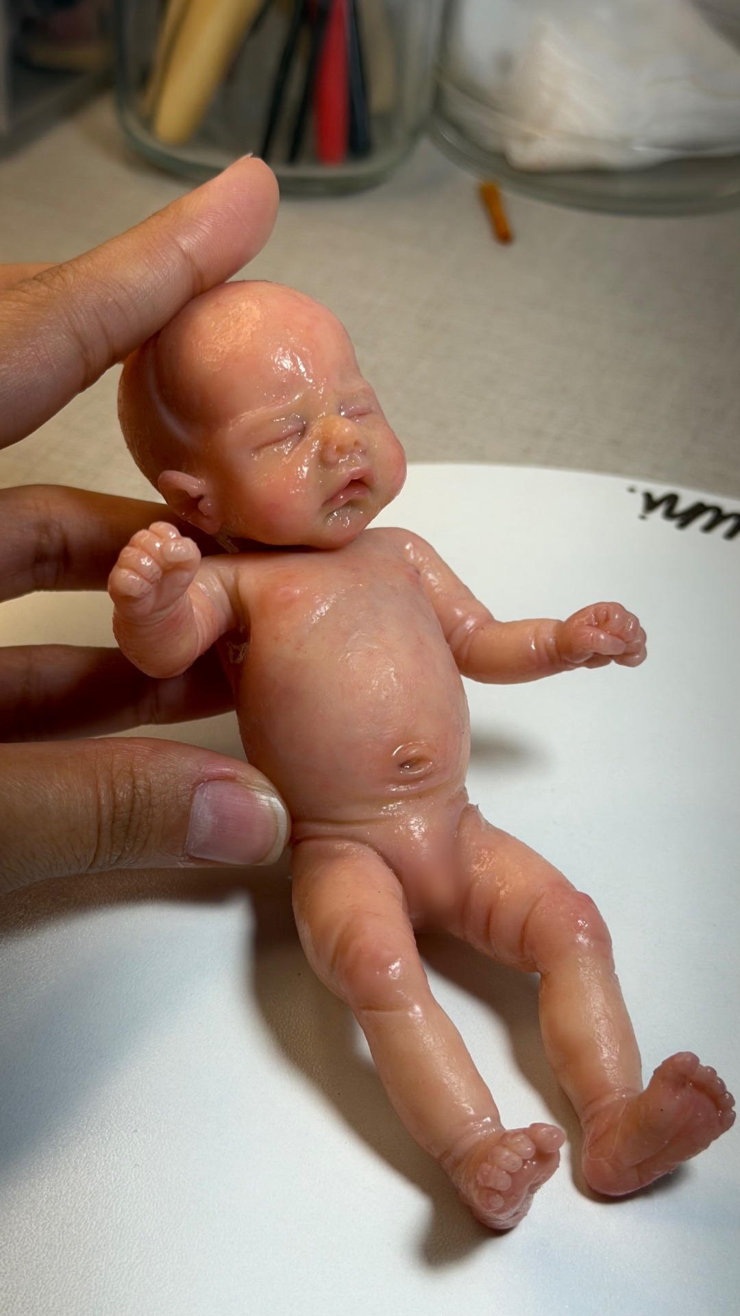 A miniature silicone baby held in the artist's hand